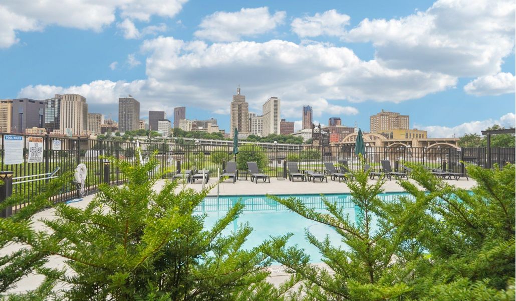 The Scenic pool with city skyline in the background under a partly cloudy sky, framed by green bushes.