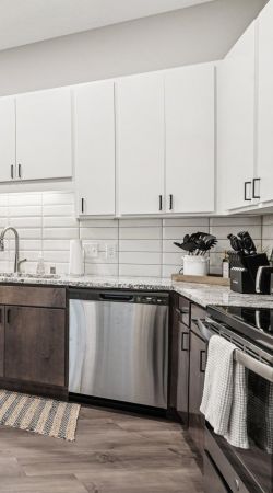 The Scenic modern kitchen with white cabinets, stainless steel appliances, and a wooden-topped island under pendant lights.