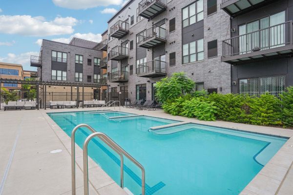 The Scenic outdoor swimming pool with metal ladders, lounge chairs, and modern apartment building in the background.