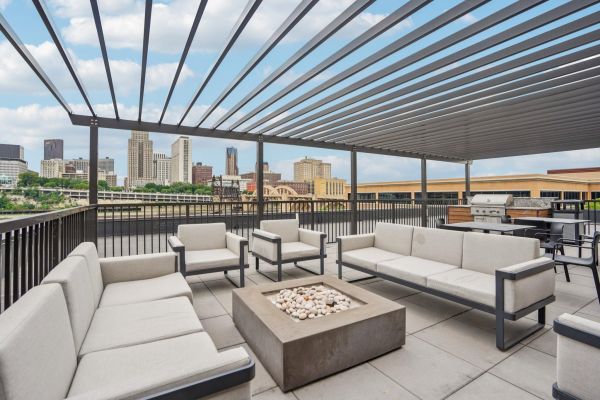 The Scenic outdoor rooftop lounge with modern seating, fire pit, and city skyline view under a pergola.